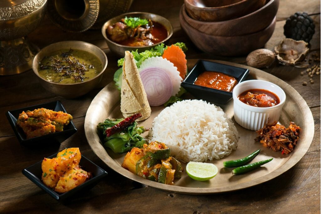 A traditional Nepali thali set with dal, rice, meat curry, vegetable sides and achar on a brass plate