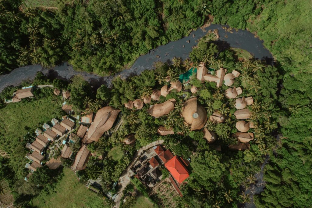 Aerial view of Fivelements Retreat Bali in Mambal, showing thatched-roof pavilions nestled among tropical jungle along the Ayung River