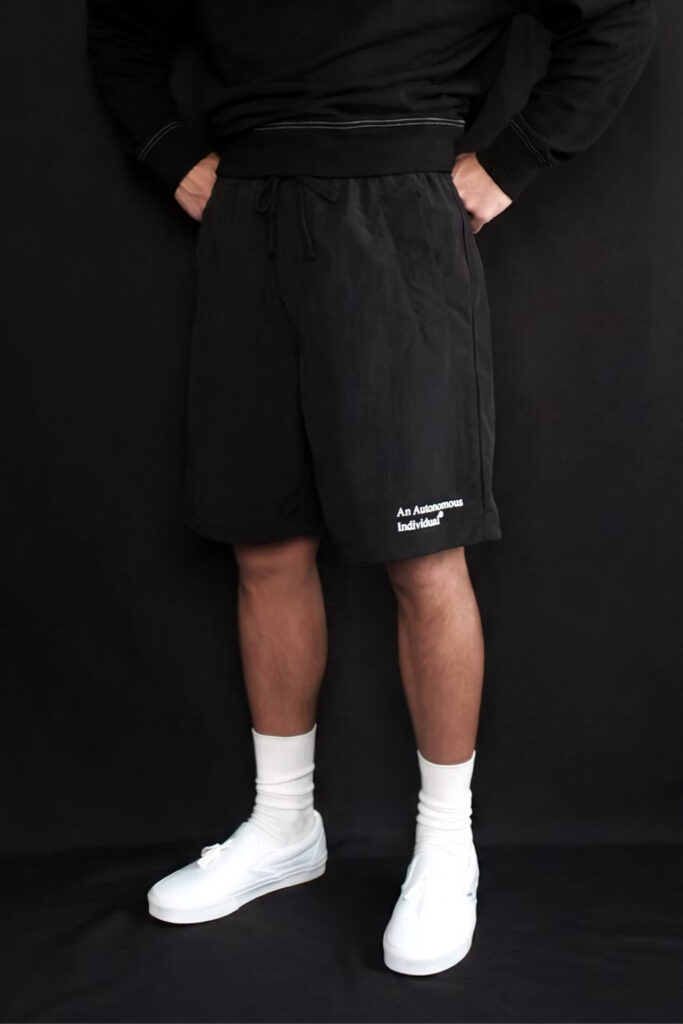aai Traverse Shorts in black, worn with a black long-sleeve top and white Vans sneakers