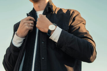 Man adjusting his jacket collar, wearing layered outerwear with a watch