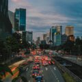 Heavy traffic on a multi-lane road in Singapore's CBD at dusk, with car light trails and the city skyline in the background