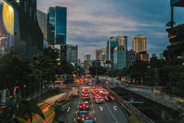 Heavy traffic on a multi-lane road in Singapore's CBD at dusk, with car light trails and the city skyline in the background