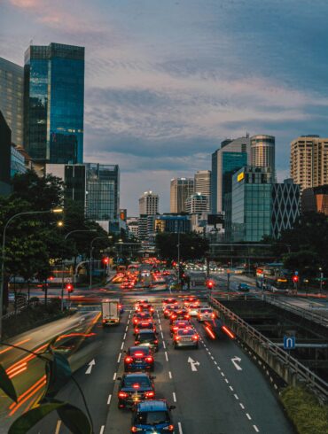 Heavy traffic on a multi-lane road in Singapore's CBD at dusk, with car light trails and the city skyline in the background