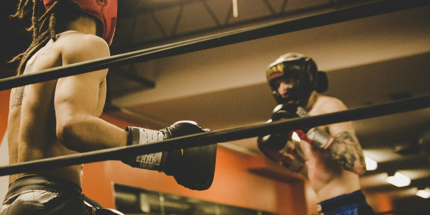 Two boxers sparring in headgear and gloves inside a boxing ring at a gymTwo boxers sparring in headgear and gloves inside a boxing ring at a gym
