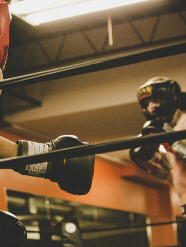 Two boxers sparring in headgear and gloves inside a boxing ring at a gymTwo boxers sparring in headgear and gloves inside a boxing ring at a gym