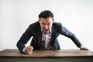 A man wearing formal suit yelling and pounding the table
