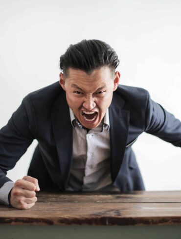 A man wearing formal suit yelling and pounding the table