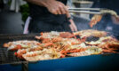 Chef grilling fresh lobsters and crabs on a large outdoor barbecue grill, with smoke rising.