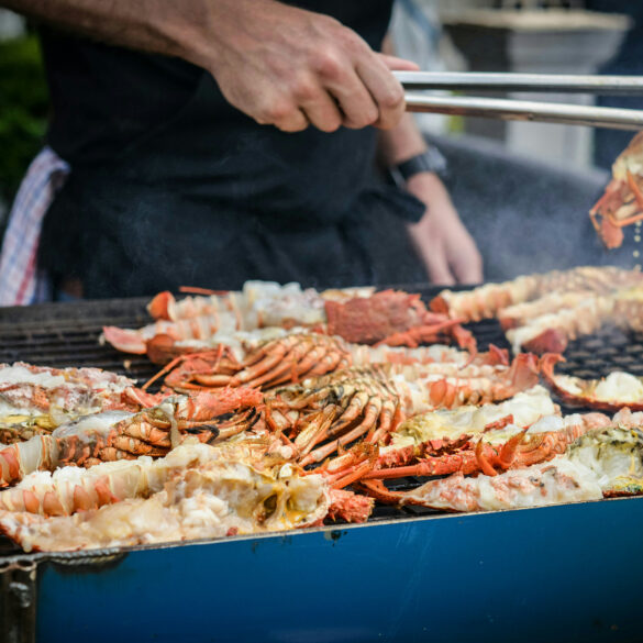 Chef grilling fresh lobsters and crabs on a large outdoor barbecue grill, with smoke rising.