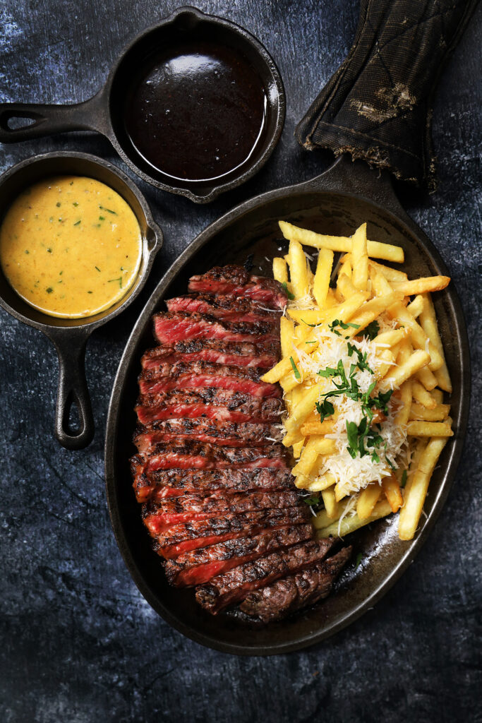 Steak Frites at Luncheon at Bedrock Bar & Grill, Singapore, featuring sliced grilled striploin with truffle parmesan fries and black pepper and Café de Paris sauces