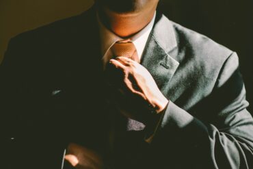 Close-up of a man in a tailored charcoal suit adjusting his tie, hand resting on the jacket's lapel