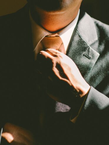 Close-up of a man in a tailored charcoal suit adjusting his tie, hand resting on the jacket's lapel