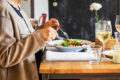 A diner enjoying a salad with a glass of white wine at a restaurant table, representing the best set lunches in Singapore