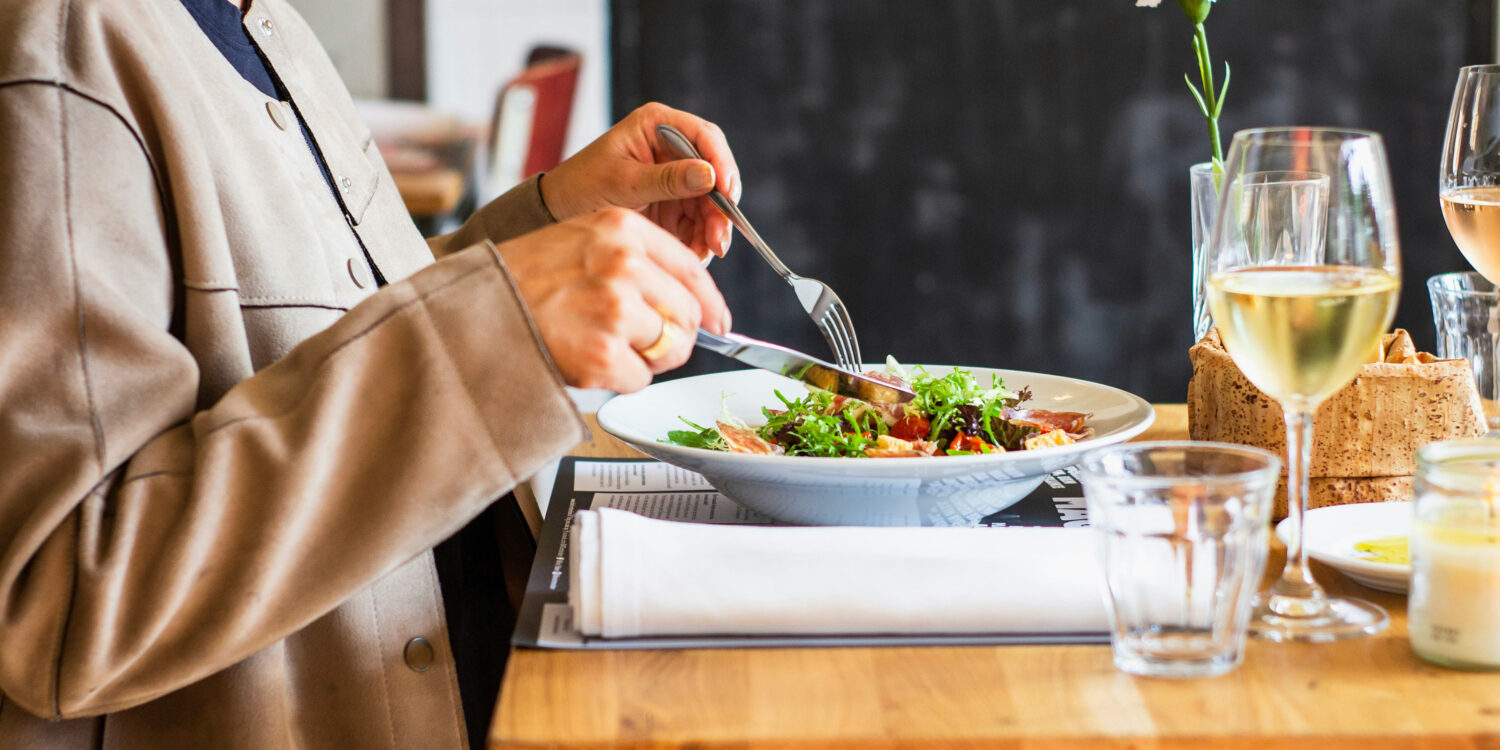 A diner enjoying a salad with a glass of white wine at a restaurant table, representing the best set lunches in Singapore