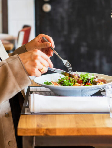 A diner enjoying a salad with a glass of white wine at a restaurant table, representing the best set lunches in Singapore