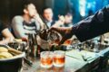 Bartender pouring craft cocktails into rocks glasses at a busy cocktail bar, showcasing mixology techniques and vibrant nightlife atmosphere in Singapore.