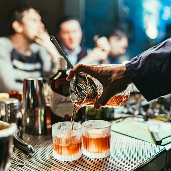 Bartender pouring craft cocktails into rocks glasses at a busy cocktail bar, showcasing mixology techniques and vibrant nightlife atmosphere in Singapore.
