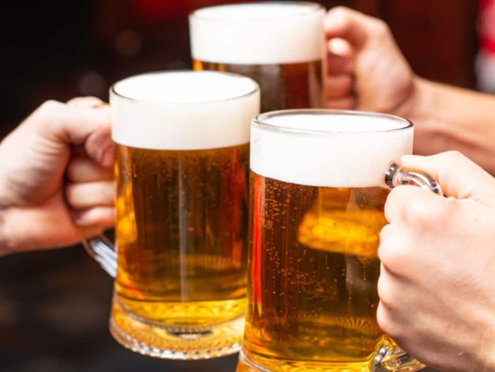Friends toasting with pints of beer at Crossroads Café, Orchard Road’s go-to happy hour spot in Singapore.