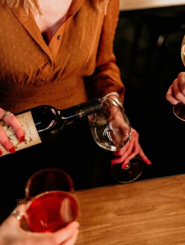 Group of friends pouring and enjoying red and white wine at a bar during happy hour in Singapore, showcasing casual nightlife and social drinking culture.