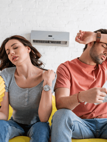 Pretty woman with hand fan and handsome man with newspaper suffering from heat at home