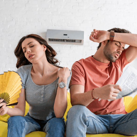 Pretty woman with hand fan and handsome man with newspaper suffering from heat at home
