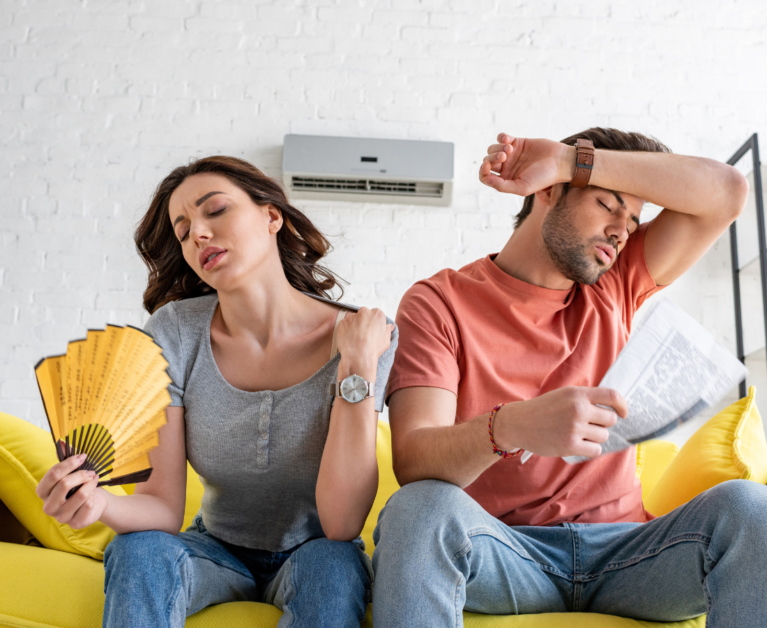 Pretty woman with hand fan and handsome man with newspaper suffering from heat at home
