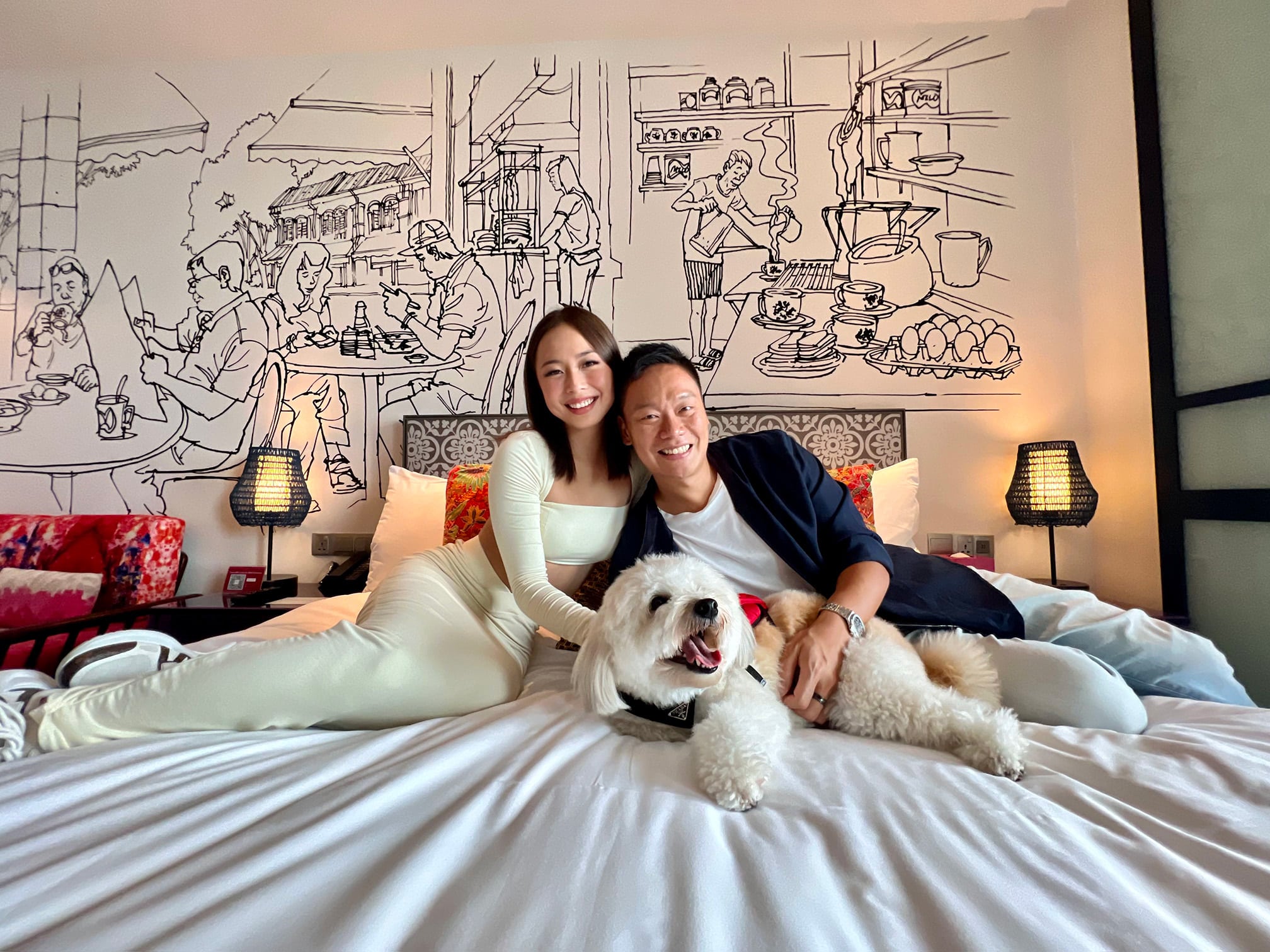 Couple smiling on a bed with their fluffy white dog at Hotel Indigo Singapore Katong, enjoying a pet-friendly staycation in a Peranakan-inspired boutique hotel.