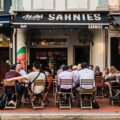 Lively outdoor dining scene at Sarnies café on Telok Ayer Street, Singapore, with diners seated at wooden tables against a backdrop of heritage shophouses.