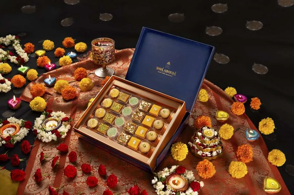 Shahi Maharani mithai box in navy and gold with rows of barfi and ladoo, surrounded by marigolds and diyas.