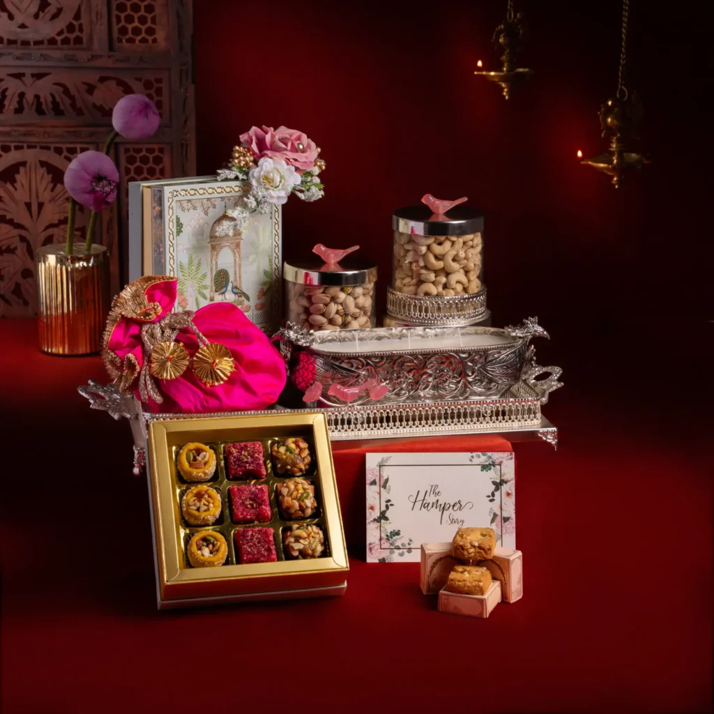 The Hamper Story Deepavali hamper with a nine-piece mithai box, jars of pistachios and cashews, and a silver candle.