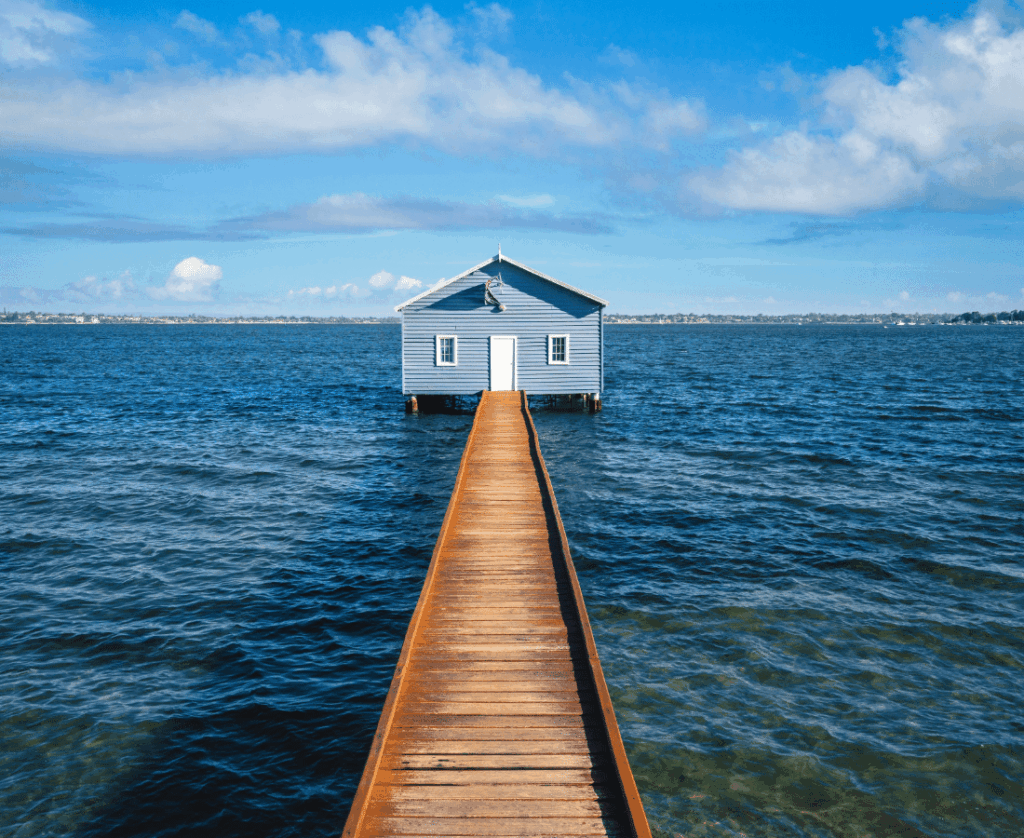 A house over the water connected to the shore by a boardwalk, on a sunny day.