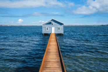 A house over the water connected to the shore by a boardwalk, on a sunny day.