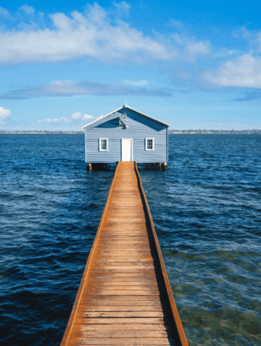 A house over the water connected to the shore by a boardwalk, on a sunny day.