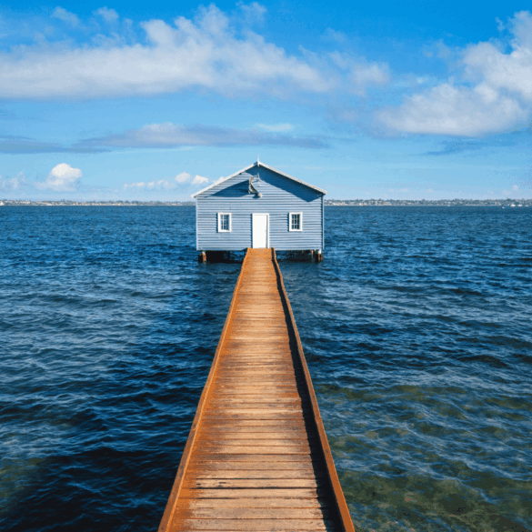 A house over the water connected to the shore by a boardwalk, on a sunny day.