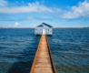 A house over the water connected to the shore by a boardwalk, on a sunny day.