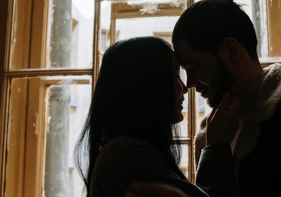 a photo of a man and woman kissing the near the window.