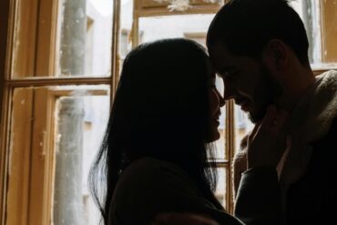 a photo of a man and woman kissing the near the window.