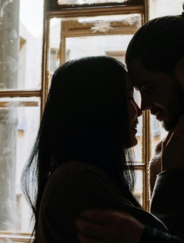 a photo of a man and woman kissing the near the window.