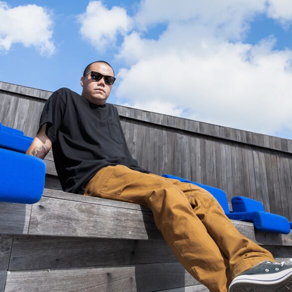 an image of archie dennis lounging at an outdoor bench, with sky and clouds above him, in his background.