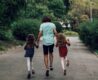 a photo of the father holding the hands of his two daughters, looking joyful from the back.