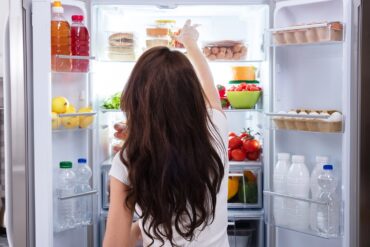 Rear View Of A Young Woman Taking Food To Eat From Refrigerator