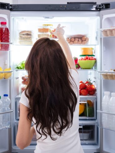Rear View Of A Young Woman Taking Food To Eat From Refrigerator
