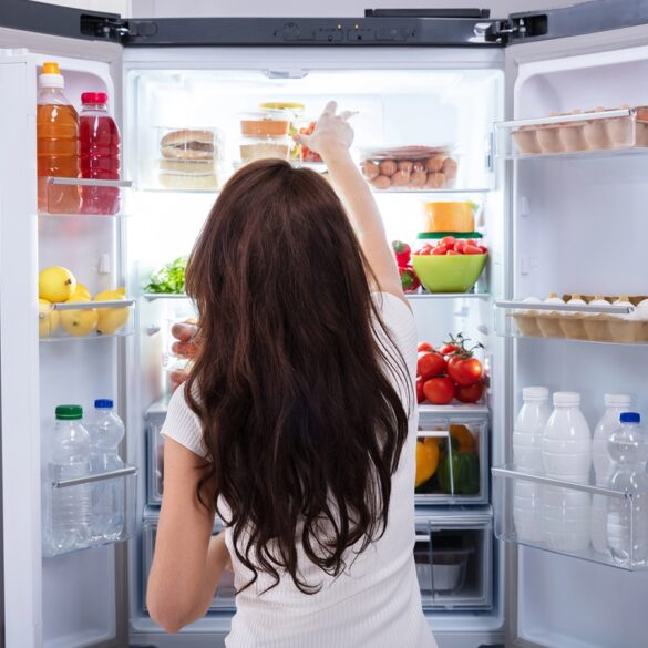 Rear View Of A Young Woman Taking Food To Eat From Refrigerator