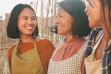 a photo of an asian mother and her two daughters having a nice time outdoors, wearing aprons cooking outside.