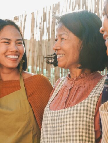 a photo of an asian mother and her two daughters having a nice time outdoors, wearing aprons cooking outside.