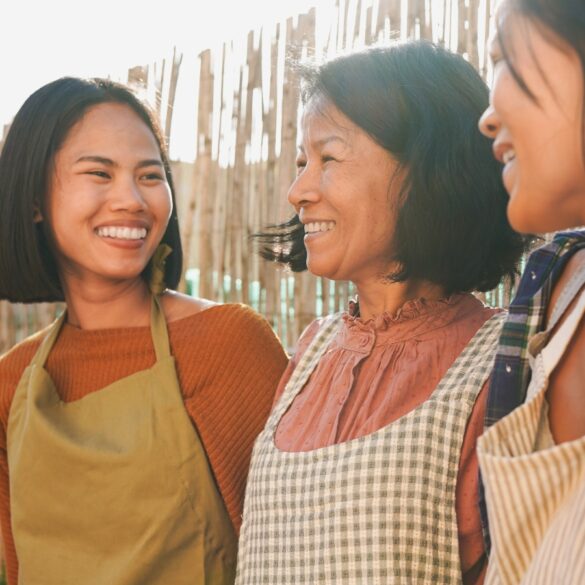 a photo of an asian mother and her two daughters having a nice time outdoors, wearing aprons cooking outside.