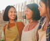 a photo of an asian mother and her two daughters having a nice time outdoors, wearing aprons cooking outside.