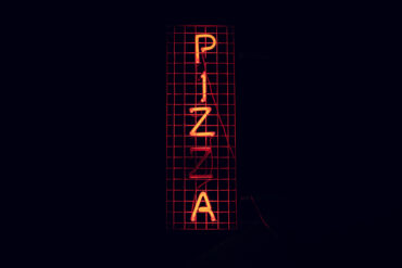An orange neon sign displaying the word "Pizza"