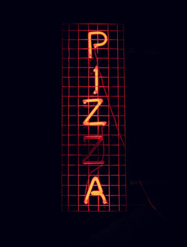 An orange neon sign displaying the word "Pizza"