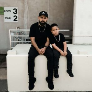 father and son sitting on a ledge, both wearing black.